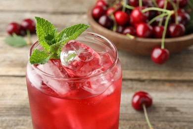 Photo of Tasty cherry soda with ice cubes, berries and mint on wooden table, closeup