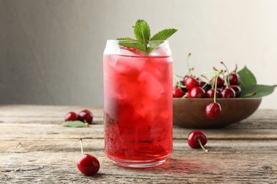 Photo of Tasty cherry soda with ice cubes, berries and mint on wooden table, closeup