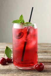 Photo of Tasty cherry soda with ice cubes, berries and mint on wooden table, closeup