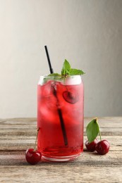 Photo of Tasty cherry soda with ice cubes, berries and mint on wooden table, closeup