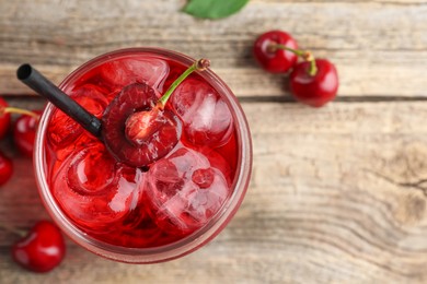 Photo of Tasty cherry soda with ice cubes and berries on wooden table, flat lay. Space for text