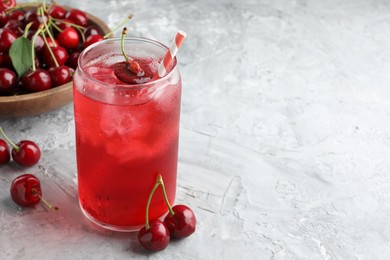 Photo of Tasty cherry soda with ice cubes and berries on grey textured table, closeup. Space for text