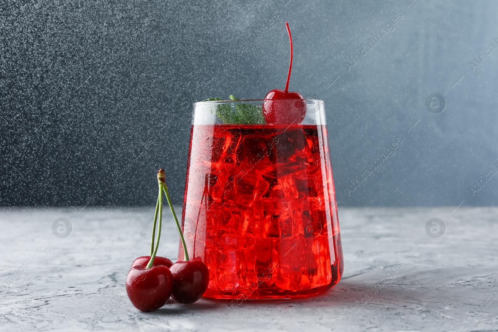 Tasty cherry soda with ice cubes, berries and mint on grey textured table, closeup Photo of Tasty cherry soda with ice cubes, berries and mint on grey textured table, closeup