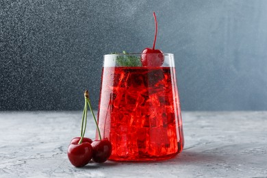 Photo of Tasty cherry soda with ice cubes, berries and mint on grey textured table, closeup
