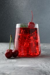 Photo of Tasty cherry soda with ice cubes, berries and mint on grey textured table, closeup