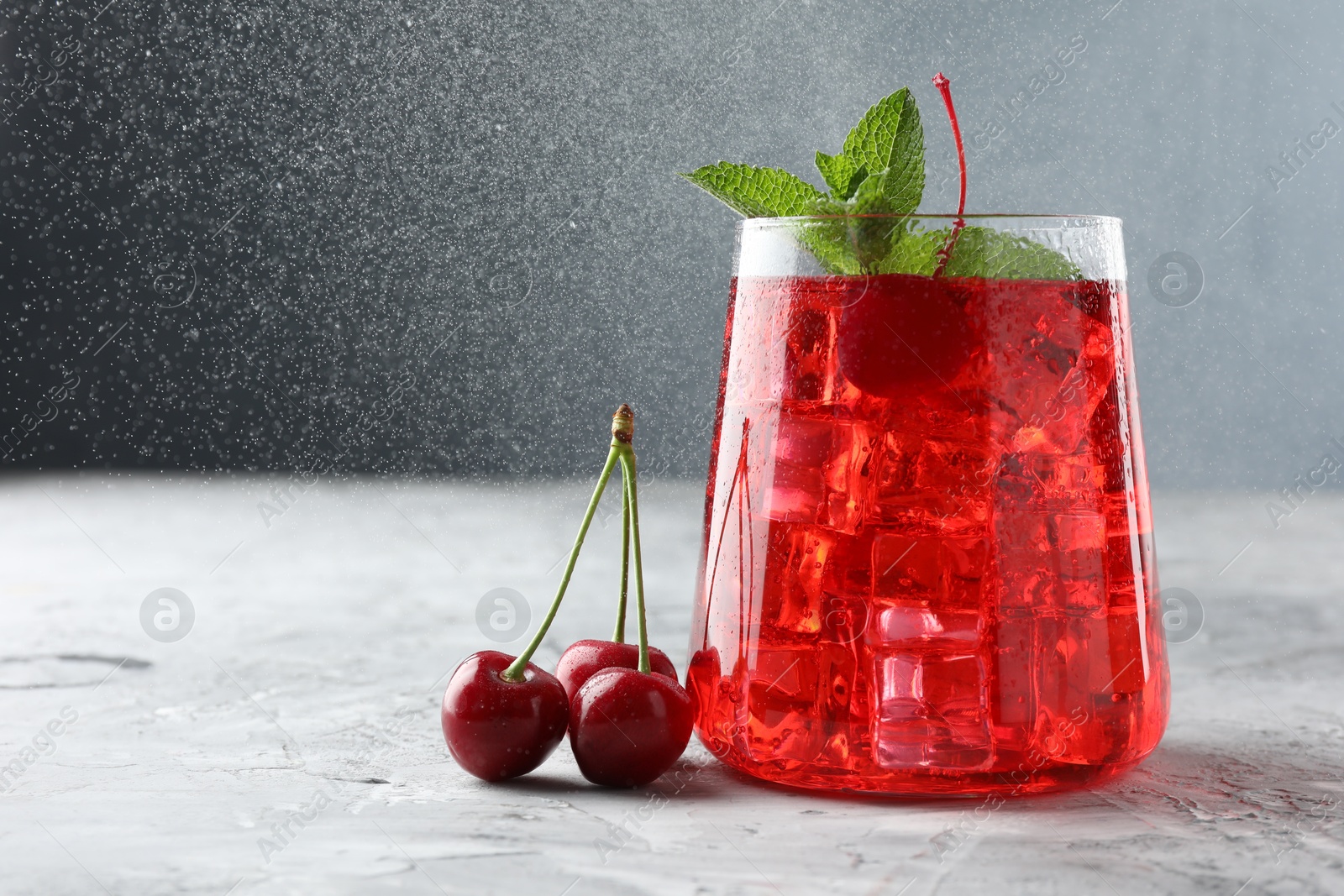 Tasty cherry soda with ice cubes, berries and mint on grey textured table, closeup. Space for text Photo of Tasty cherry soda with ice cubes, berries and mint on grey textured table, closeup. Space for text