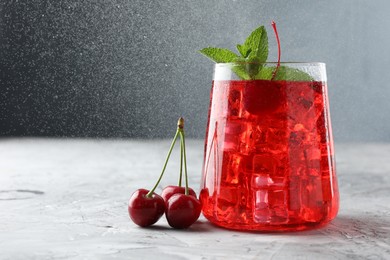 Photo of Tasty cherry soda with ice cubes, berries and mint on grey textured table, closeup. Space for text