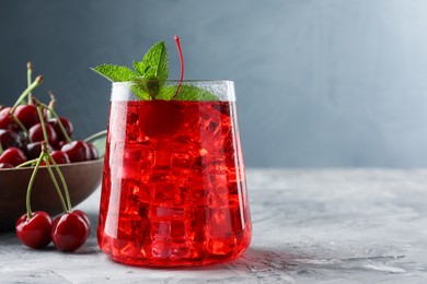 Photo of Tasty cherry soda with ice cubes, berries and mint on grey textured table, closeup. Space for text