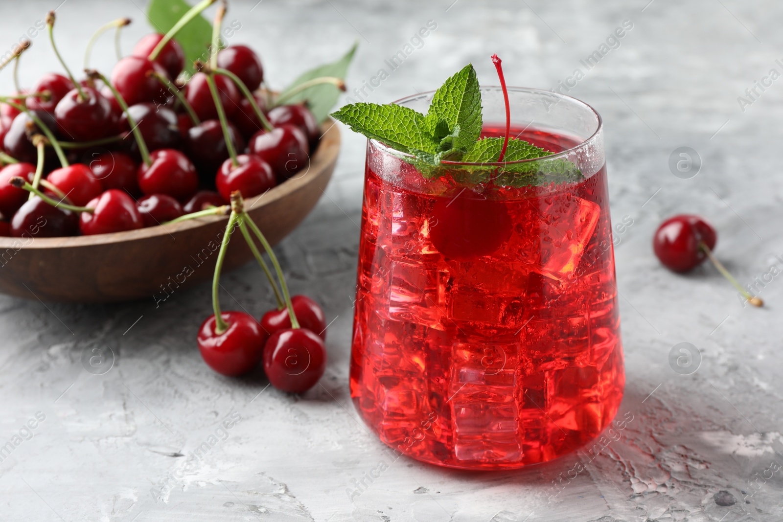Tasty cherry soda with ice cubes, berries and mint on grey textured table, closeup Photo of Tasty cherry soda with ice cubes, berries and mint on grey textured table, closeup