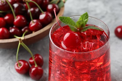 Photo of Tasty cherry soda with ice cubes, berries and mint on grey textured table, closeup