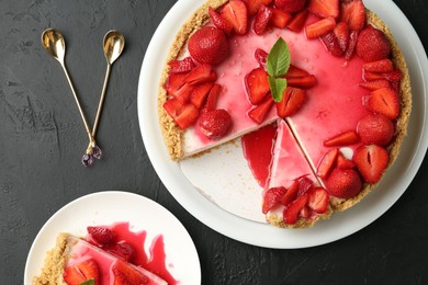 Photo of Delicious cheesecake with strawberries, sauce and mint on black table, flat lay