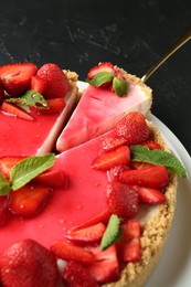 Photo of Delicious cheesecake with strawberries, sauce and mint on black table, above view