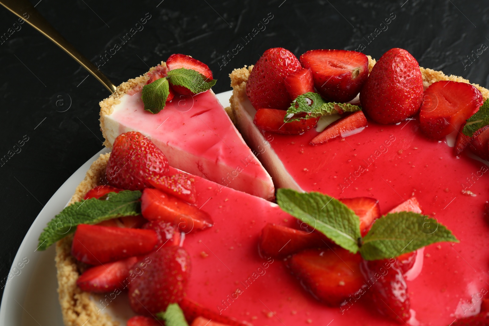 Photo of Delicious cheesecake with strawberries, sauce and mint on black table, closeup