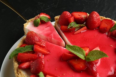 Photo of Delicious cheesecake with strawberries, sauce and mint on black table, closeup