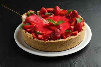 Photo of Delicious cheesecake with strawberries, sauce and mint on black table, closeup