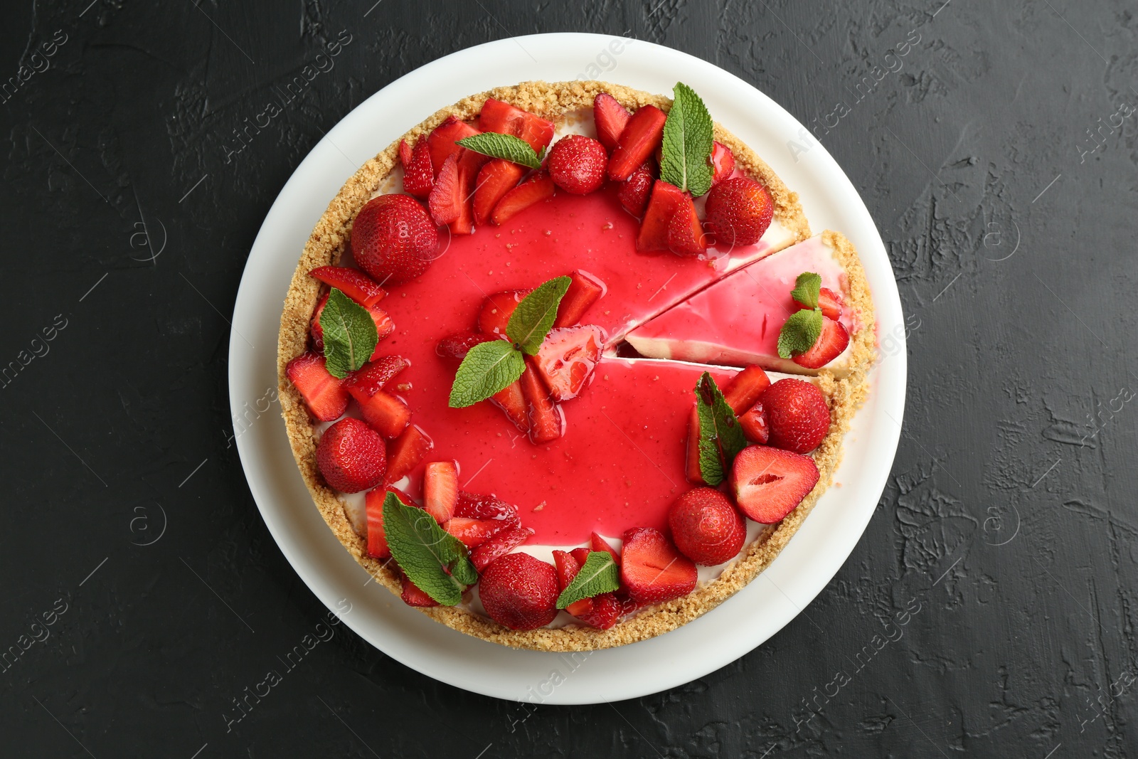Photo of Delicious cheesecake with strawberries, sauce and mint on black table, top view