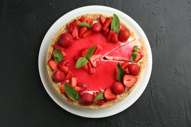 Photo of Delicious cheesecake with strawberries, sauce and mint on black table, top view