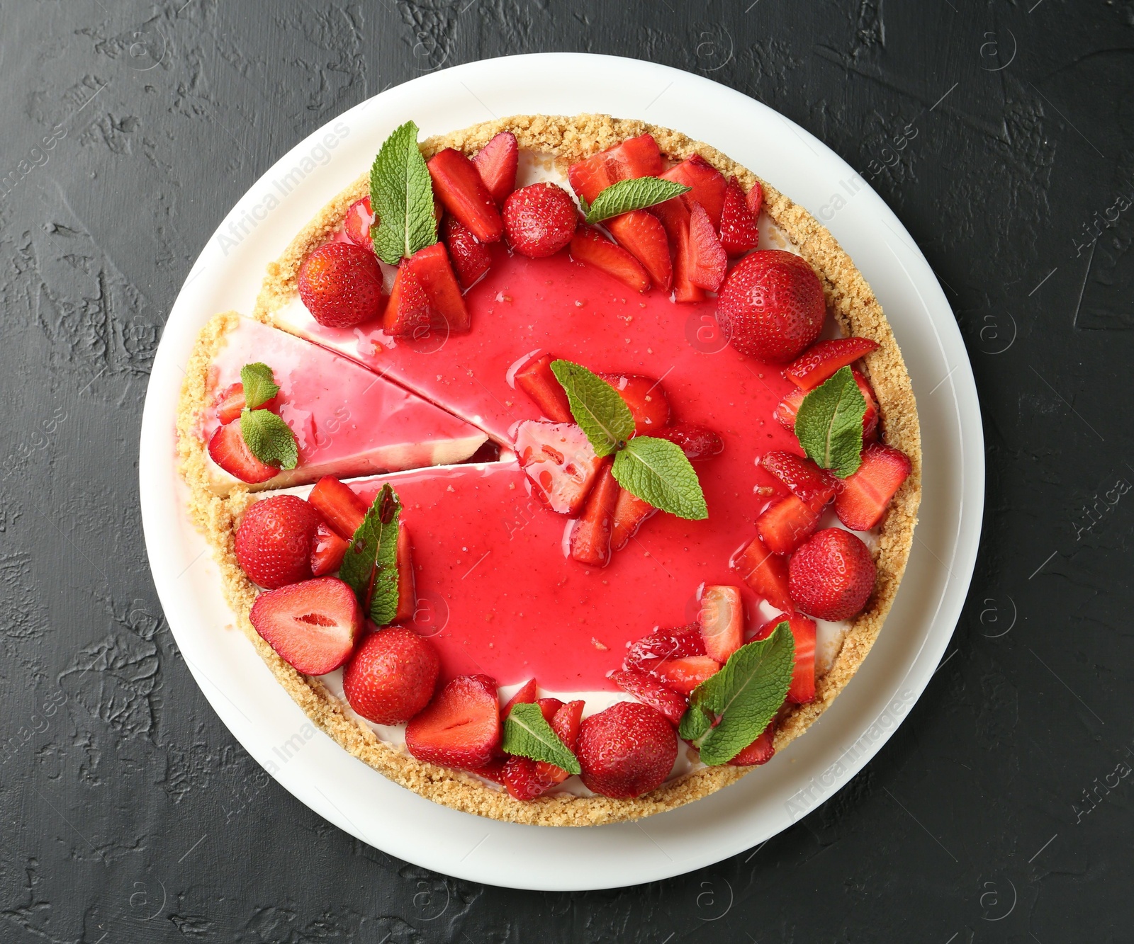 Photo of Delicious cheesecake with strawberries, sauce and mint on black table, top view