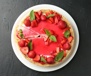 Photo of Delicious cheesecake with strawberries, sauce and mint on black table, top view