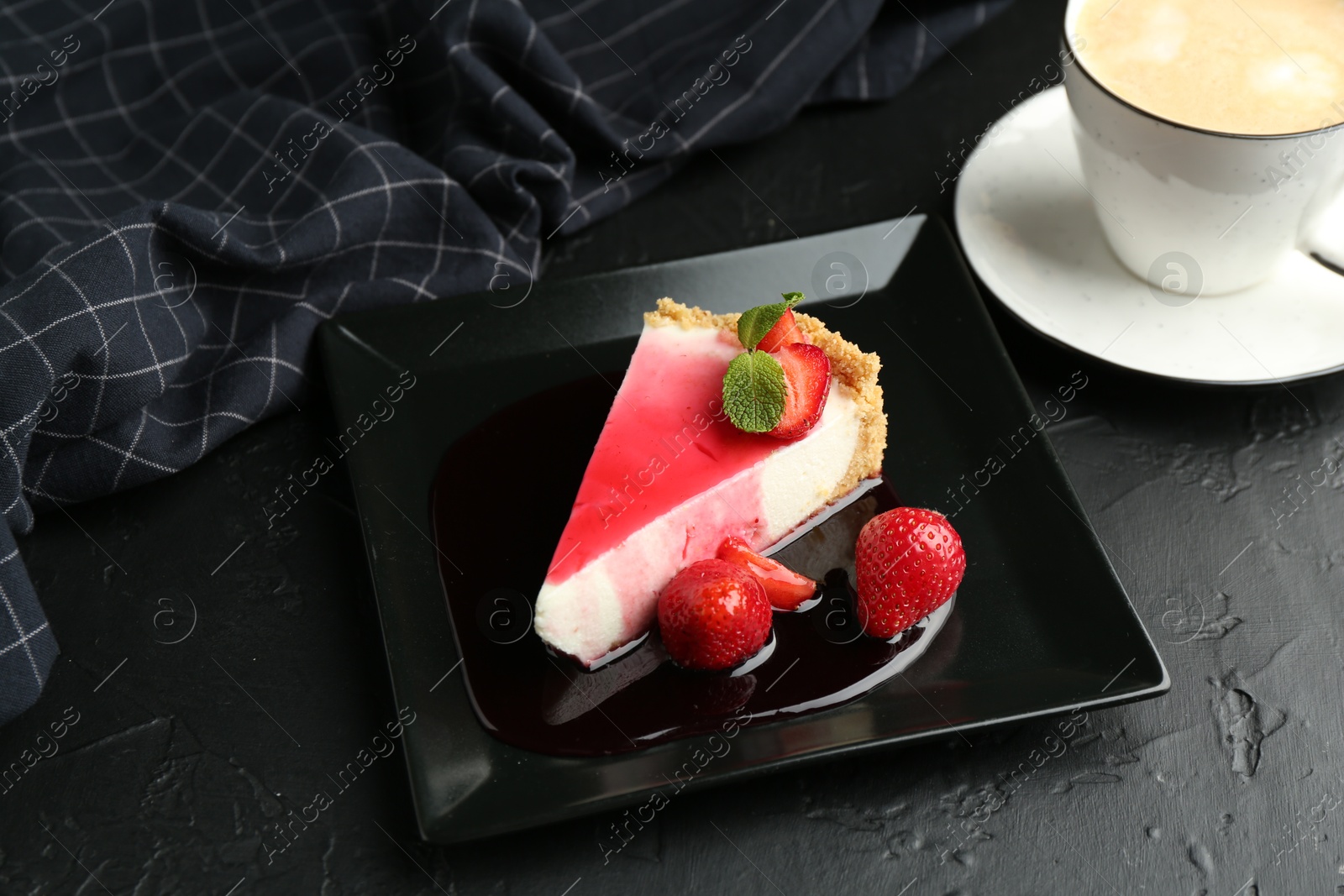 Photo of Piece of tasty cheesecake with strawberries, sauce, mint and coffee on black table, above view