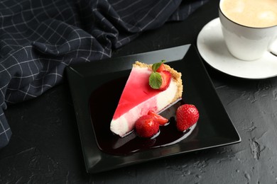 Photo of Piece of tasty cheesecake with strawberries, sauce, mint and coffee on black table, above view