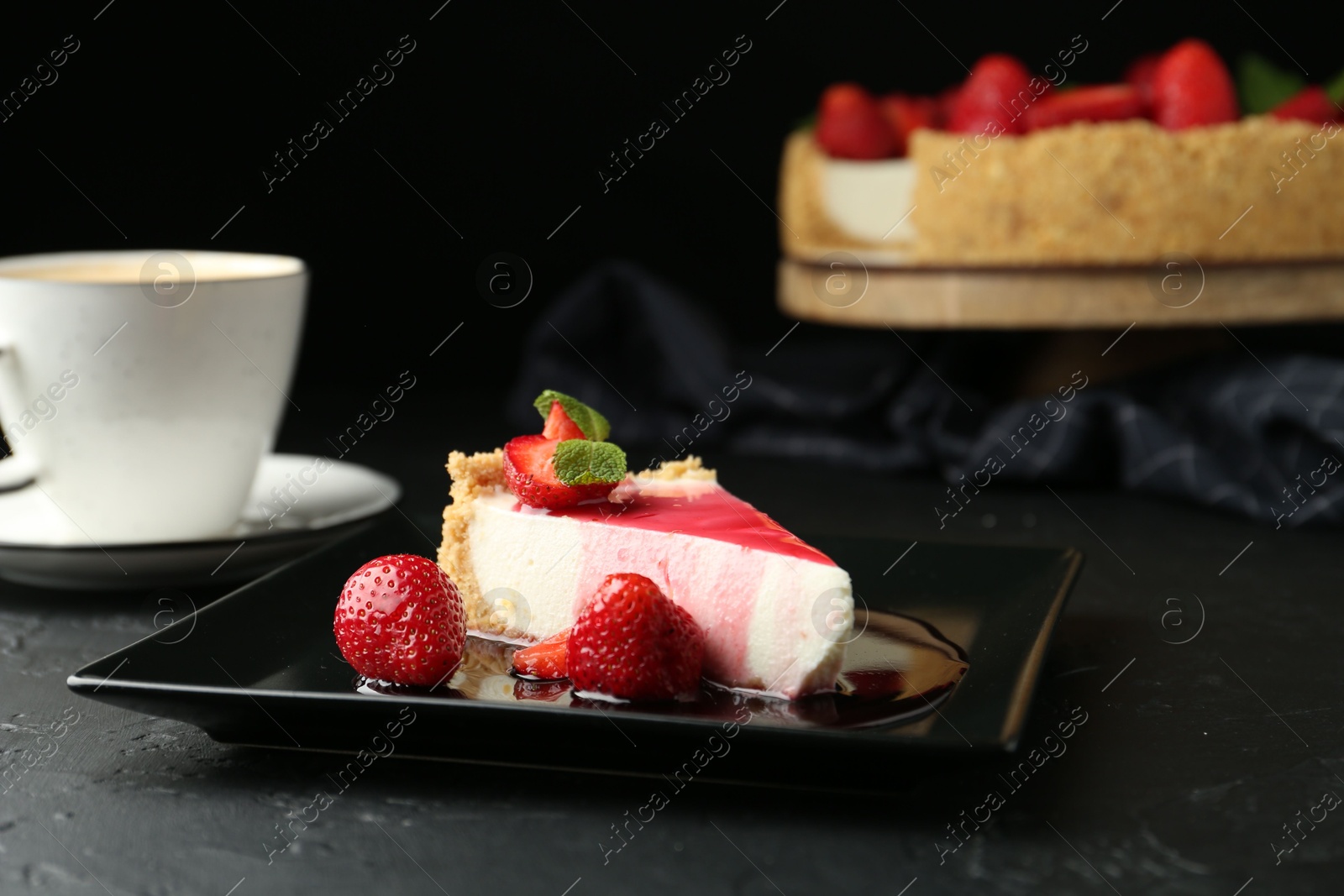 Photo of Piece of tasty cheesecake with strawberries, sauce, mint and coffee on black table, closeup