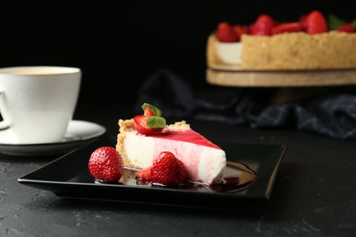 Photo of Piece of tasty cheesecake with strawberries, sauce, mint and coffee on black table, closeup
