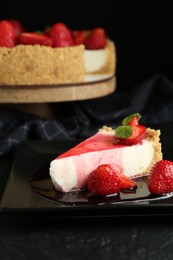 Photo of Delicious cheesecake with strawberries, sauce and mint on black table, closeup