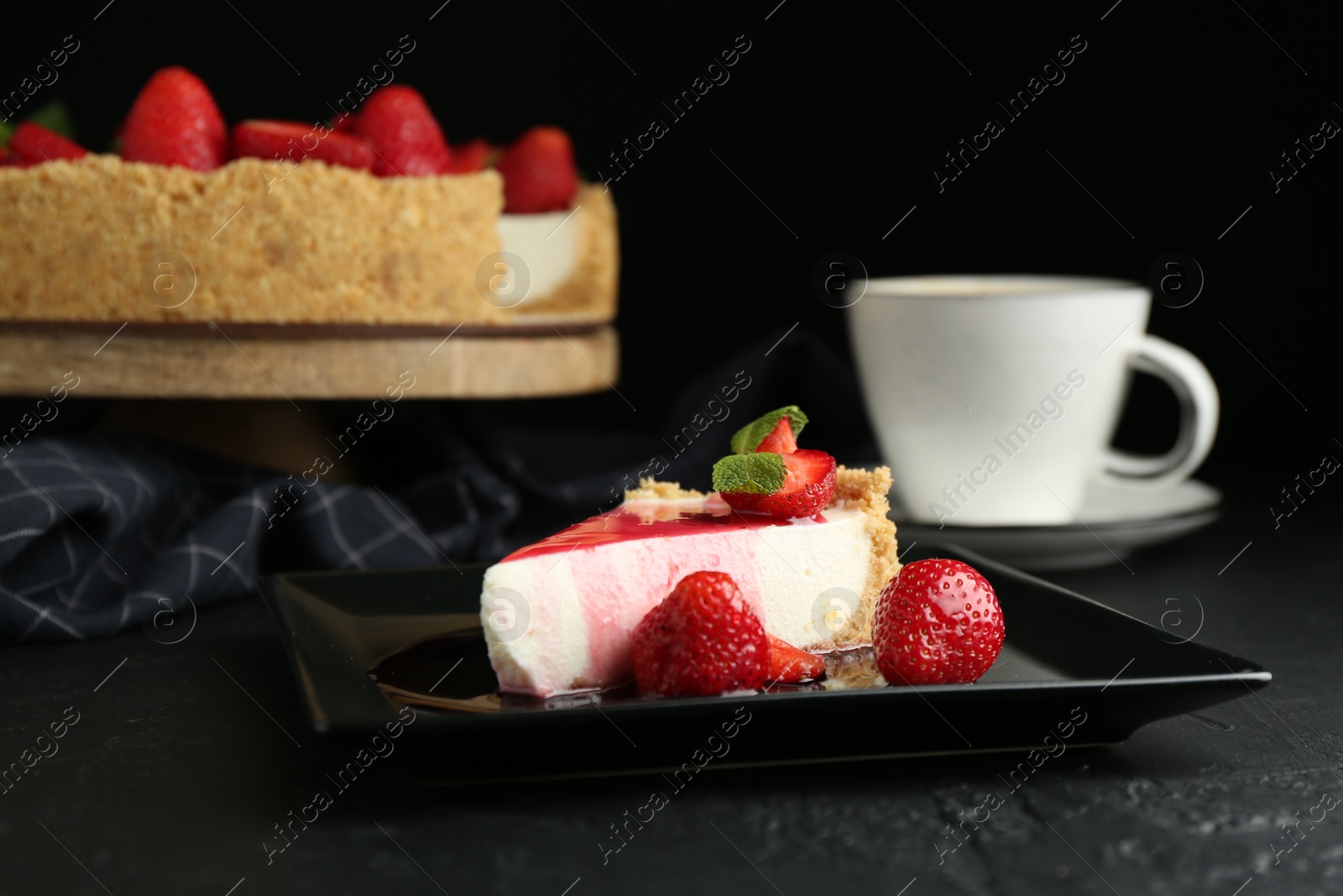 Photo of Piece of tasty cheesecake with strawberries, sauce, mint and coffee on black table, closeup