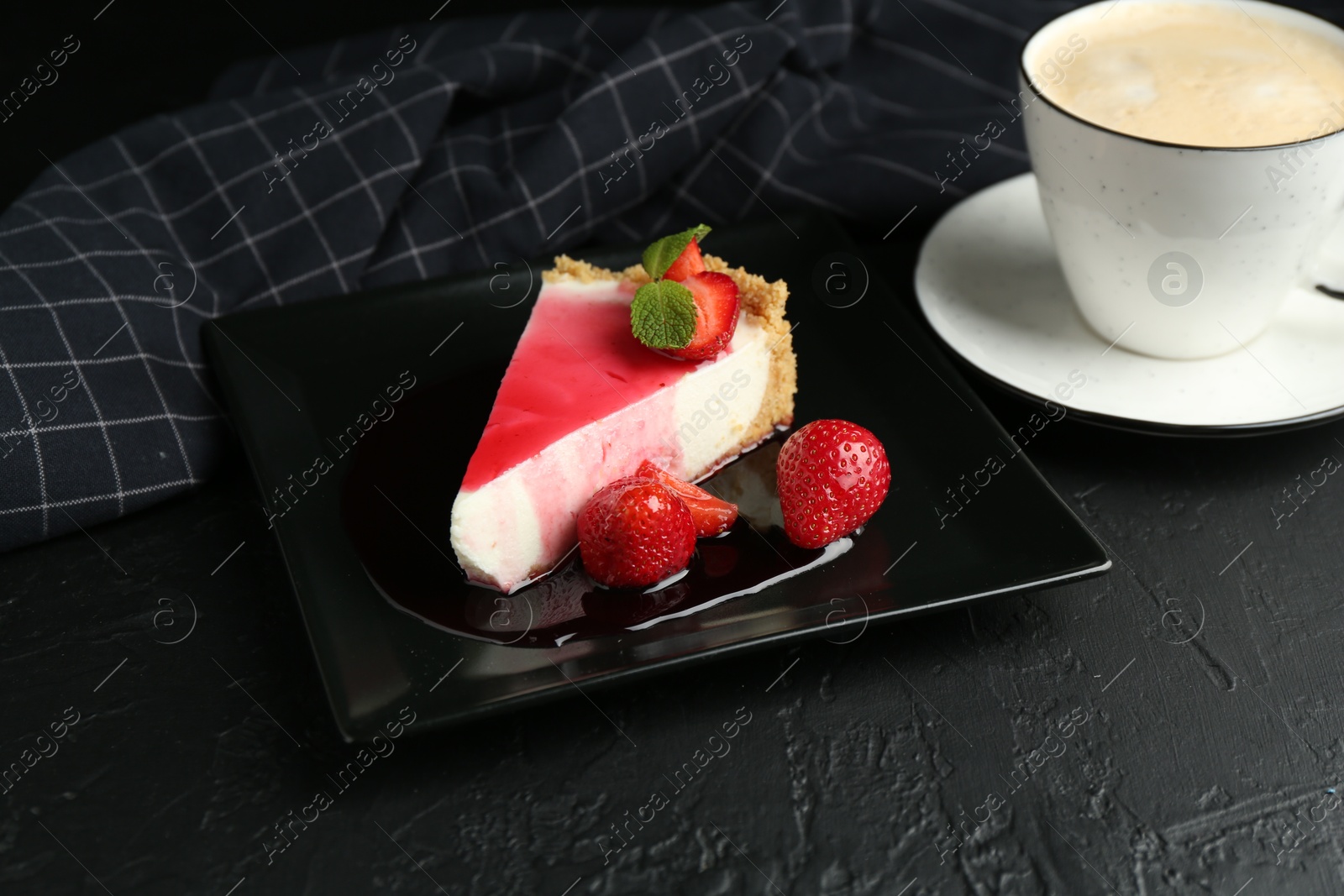 Photo of Piece of tasty cheesecake with strawberries, sauce, mint and coffee on black table, closeup
