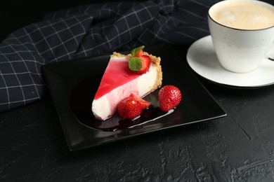 Photo of Piece of tasty cheesecake with strawberries, sauce, mint and coffee on black table, closeup
