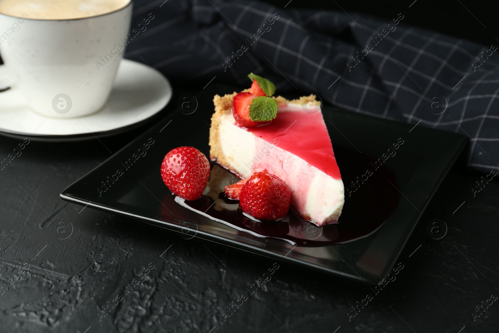 Photo of Piece of tasty cheesecake with strawberries, sauce, mint and coffee on black table, closeup
