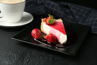 Photo of Piece of tasty cheesecake with strawberries, sauce, mint and coffee on black table, closeup
