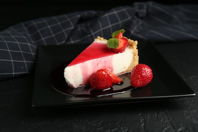 Photo of Piece of tasty cheesecake with strawberries, sauce and mint on black table, closeup