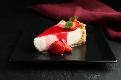 Photo of Piece of tasty cheesecake with strawberries, sauce and mint on black table, closeup