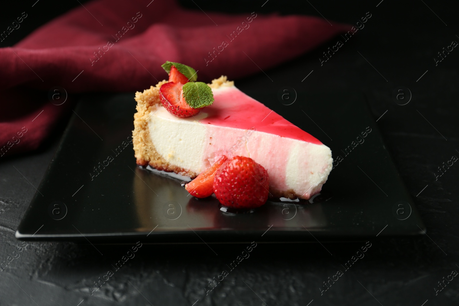 Photo of Piece of tasty cheesecake with strawberries, sauce and mint on black table, closeup