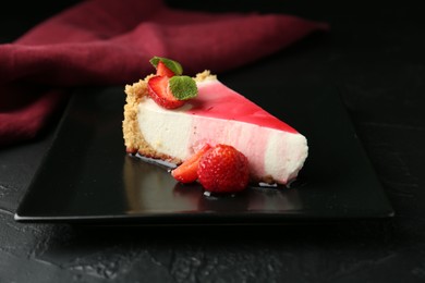Photo of Piece of tasty cheesecake with strawberries, sauce and mint on black table, closeup