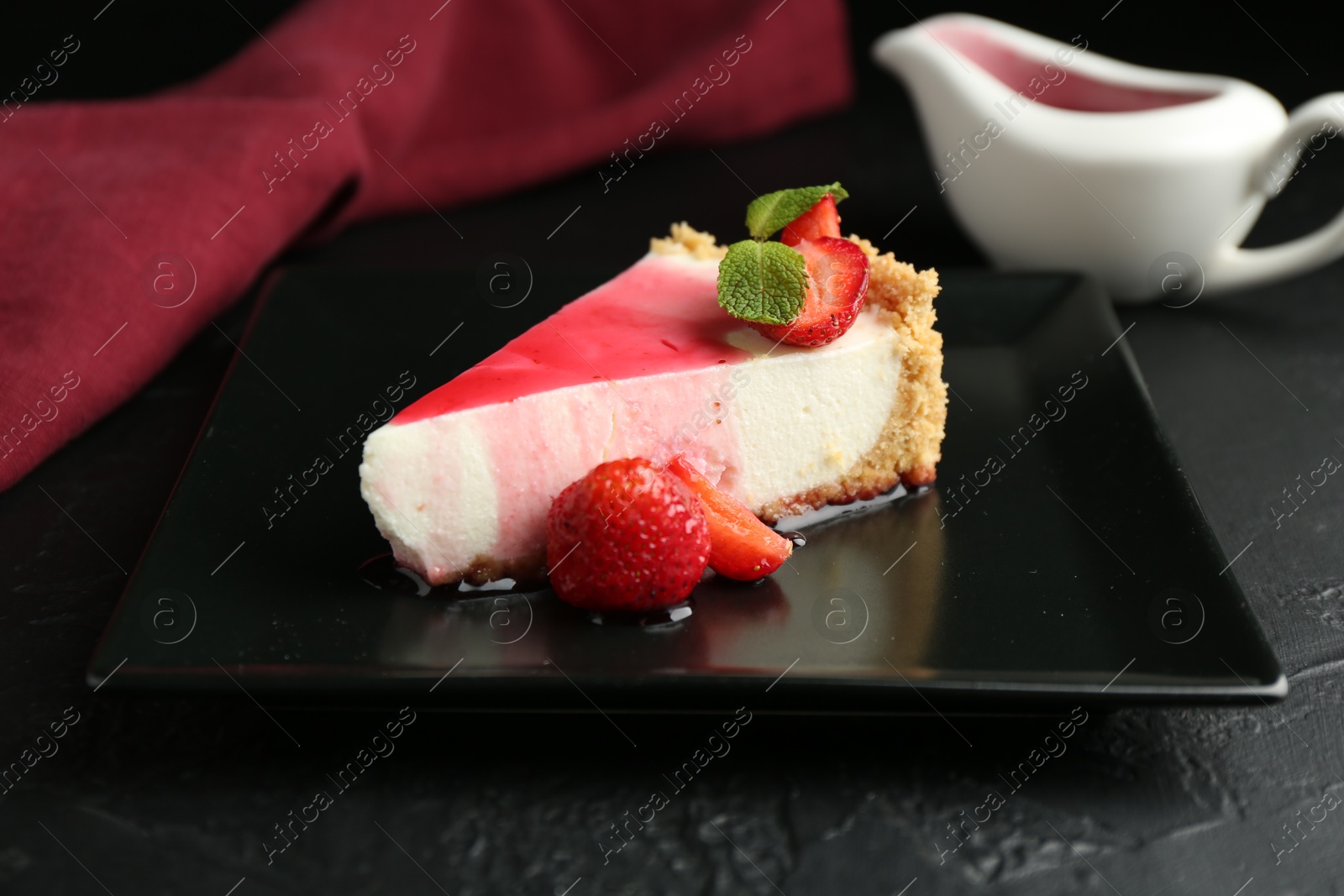 Photo of Piece of tasty cheesecake with strawberries, sauce and mint on black table, closeup