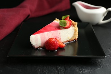 Photo of Piece of tasty cheesecake with strawberries, sauce and mint on black table, closeup