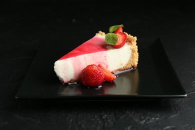 Photo of Piece of tasty cheesecake with strawberries, sauce and mint on black table, closeup