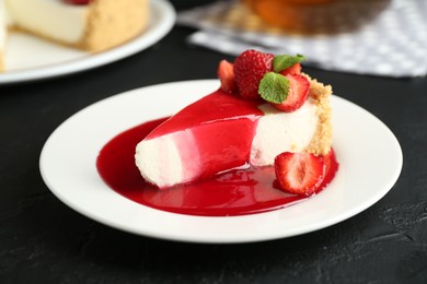 Photo of Piece of tasty cheesecake with strawberries, sauce and mint on black table, closeup