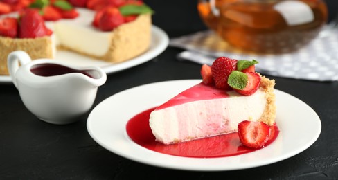 Photo of Piece of tasty cheesecake with strawberries, sauce and mint on black table, closeup