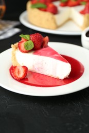 Photo of Piece of tasty cheesecake with strawberries, sauce and mint on black table, closeup