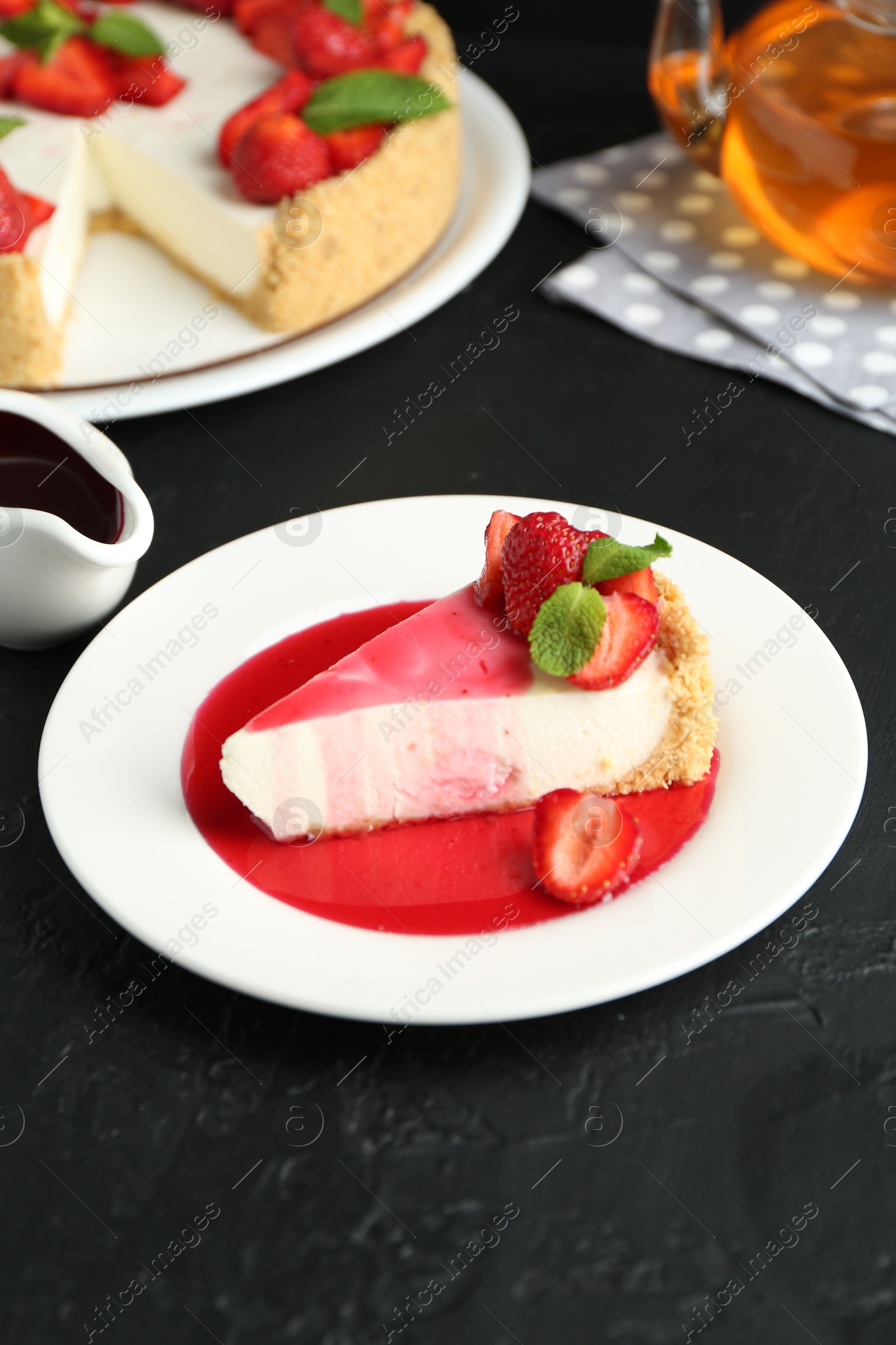 Photo of Piece of tasty cheesecake with strawberries, sauce and mint on black table, closeup