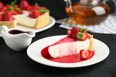 Photo of Piece of tasty cheesecake with strawberries, sauce and mint on black table, closeup
