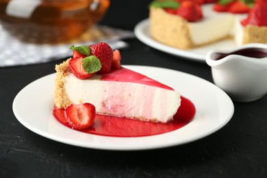 Photo of Piece of tasty cheesecake with strawberries, sauce and mint on black table, closeup