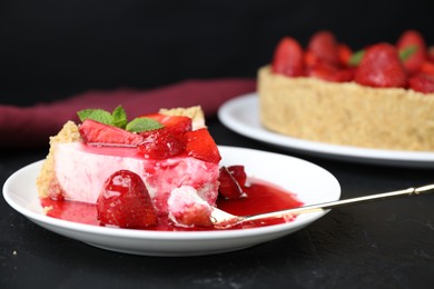 Photo of Piece of tasty cheesecake with strawberries, sauce and mint on black table, closeup