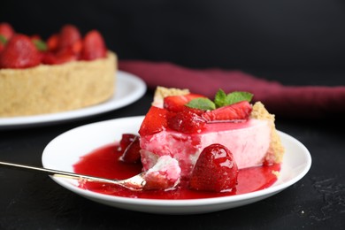Photo of Piece of tasty cheesecake with strawberries, sauce and mint on black table, closeup