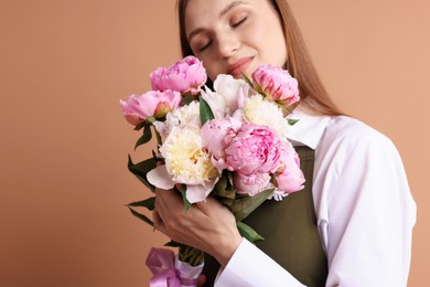 Photo of Florist with beautiful bouquet of peonies on dark beige background, space for text