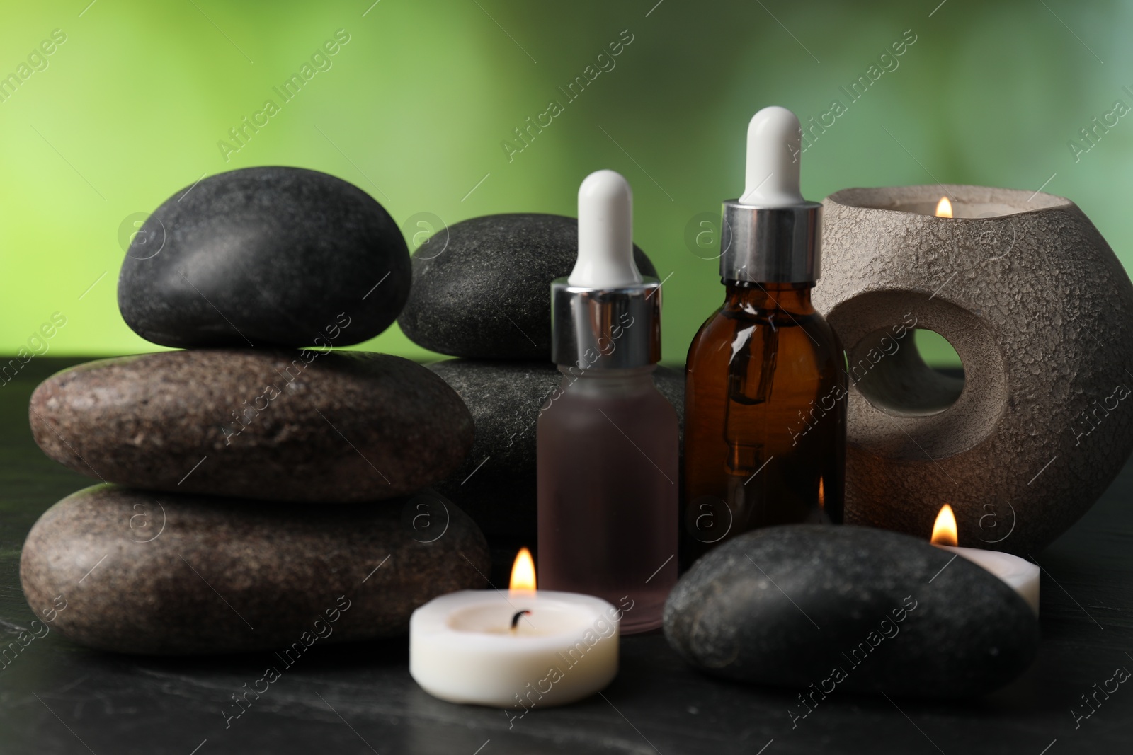 Spa composition with stones, droppers and burning candles on dark table against blurred green background, closeup Photo of Spa composition with stones, droppers and burning candles on dark table against blurred green background, closeup